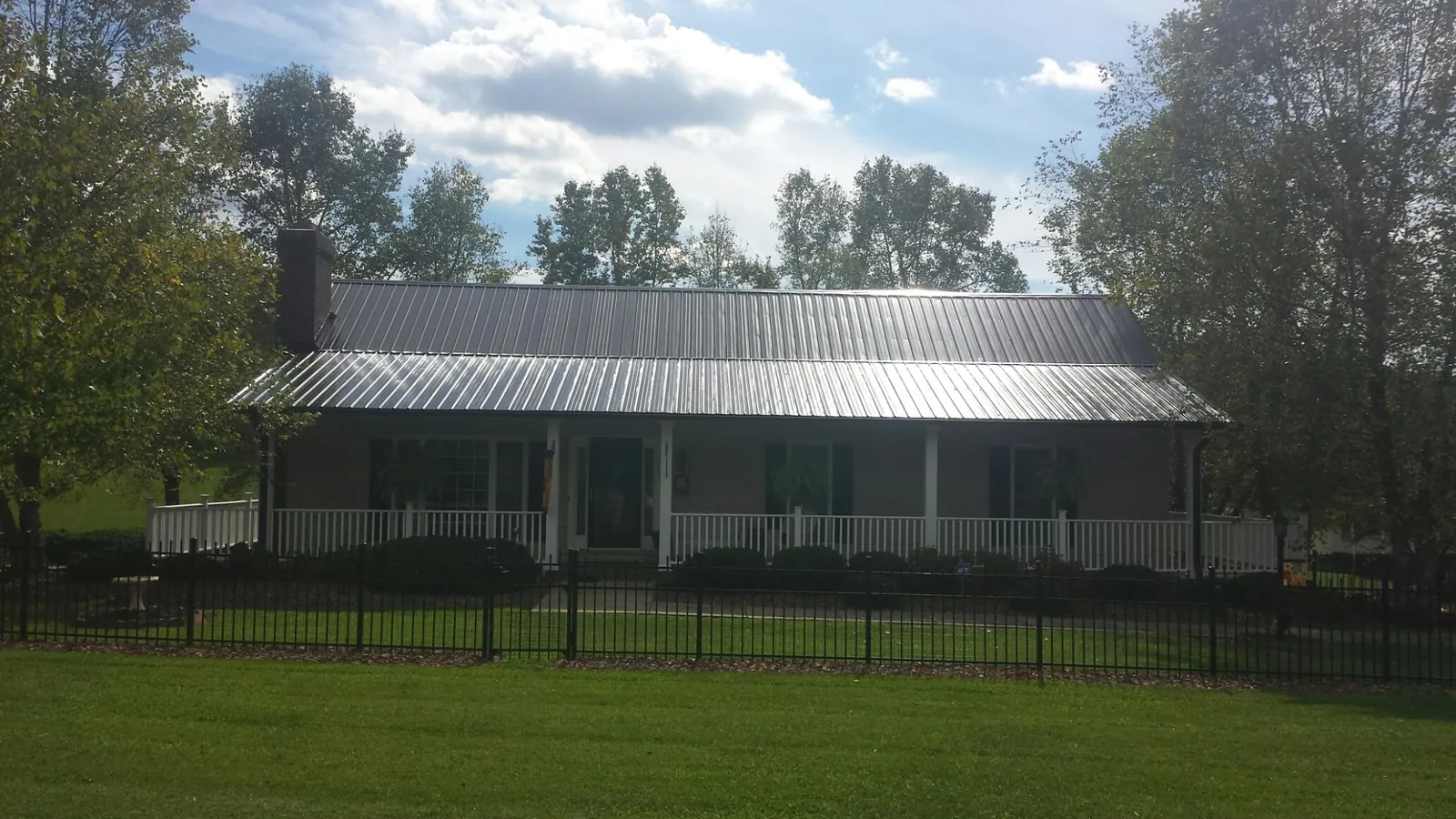 Gray metal roof on a brick ranch with a full width front porch — Gutter Guard Installation work by our crew in Lyons